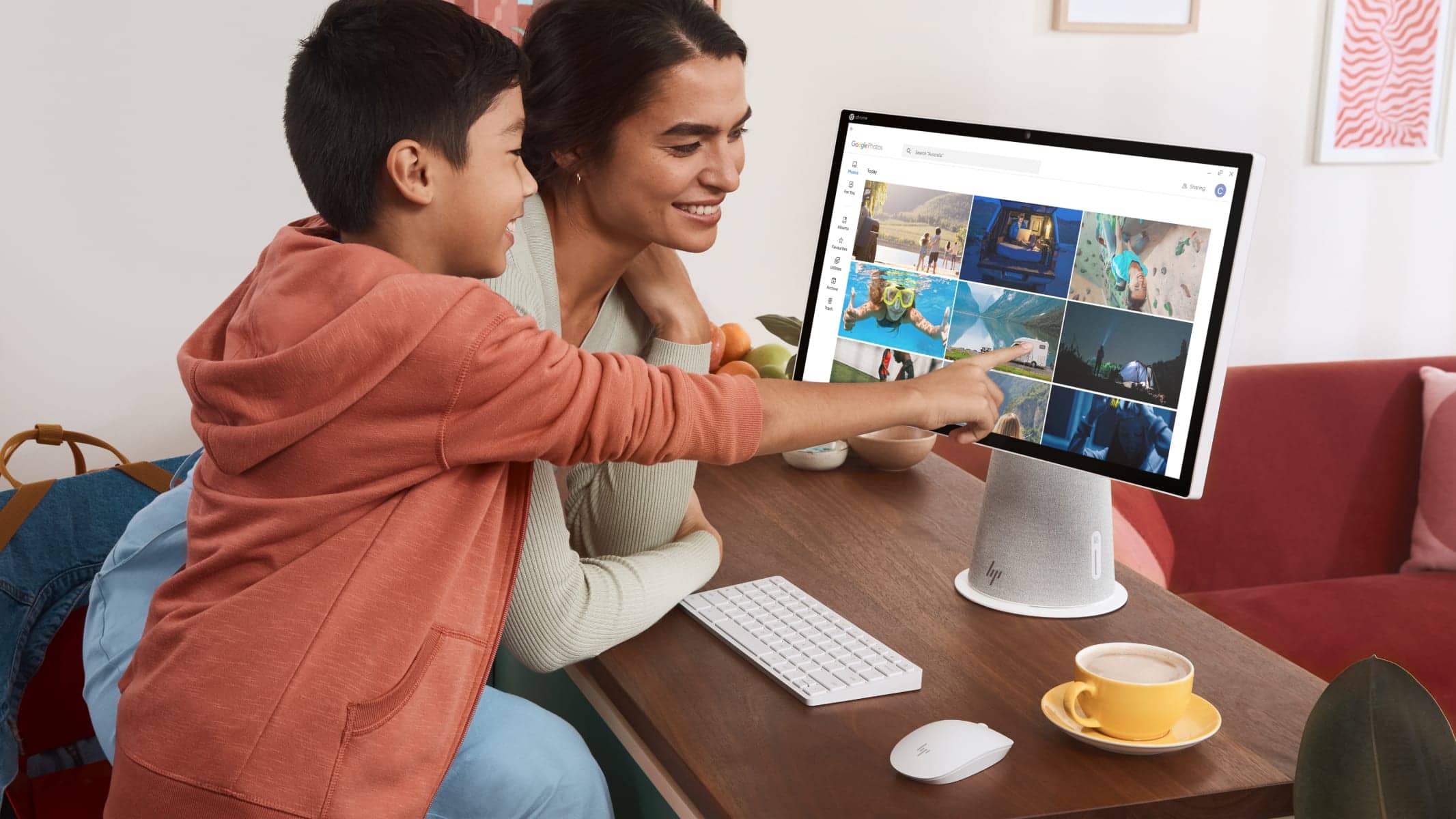 A parent and child sit at a desk looking at the Chromebase. The child is touching the screen.
